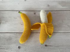 two crocheted bananas sitting next to each other on a wooden table with white boards