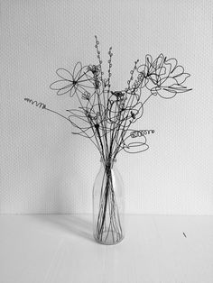 black and white photograph of dried flowers in a glass vase on a wooden table against a textured wall