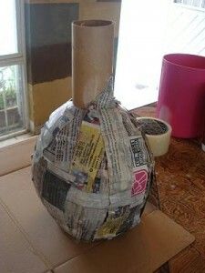 a vase made out of newspaper sitting on top of a cardboard box next to a window