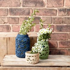 three crocheted vases with flowers in them sitting on a wooden table next to a brick wall