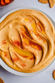 a bowl filled with hummus and carrots next to crackers