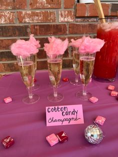 three champagne flutes are sitting on a purple tablecloth with candy cubes and cotton candy