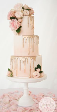 a three tiered wedding cake with pink flowers on the top and dripping icing