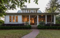 a white house sitting on top of a lush green field next to a tree and grass covered walkway