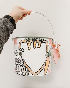 a person holding a bucket with carrots painted on it and another hand reaching for the basket