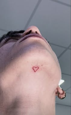 a man with a small heart tattoo on his left side behind his ear is looking up at the ceiling