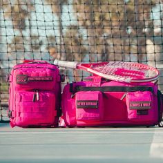 pink luggage and tennis racket are sitting on the ground in front of a net