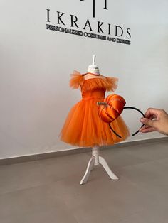 a mannequin dressed in an orange tulle dress is being held by a hand