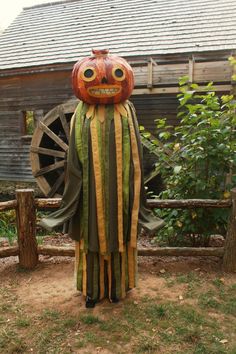 a scarecrow with a pumpkin head on it's head is standing in front of a wooden fence