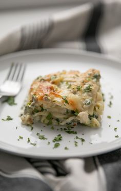 a white plate topped with lasagna covered in cheese and herbs next to a fork