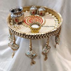 a tray with jewelry on it sitting on a white cloth covered table next to a silver cup