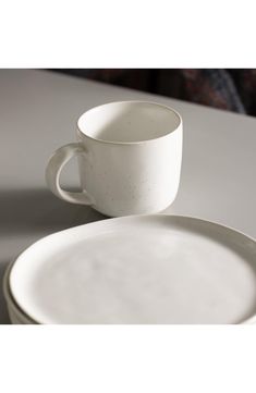 a white cup and saucer sitting on top of a table next to each other