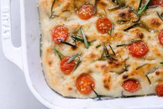 a white casserole dish with tomatoes and herbs on top, ready to be eaten