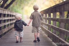 two young boys holding hands while walking on a bridge