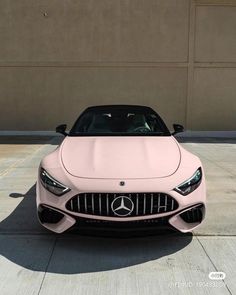 the front end of a pink car parked in a parking lot with no one around