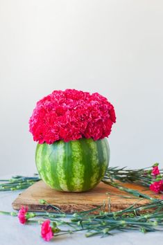 a watermelon with pink flowers in it sitting on a cutting board next to greenery