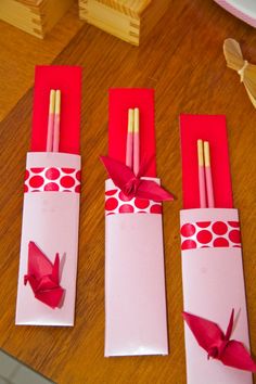 three red candles are wrapped in pink paper and tied with gold colored ribbon on a wooden table