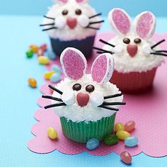 three cupcakes decorated with bunny ears and candy on a blue tablecloth background