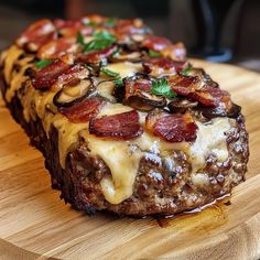 a piece of meatloaf with cheese and bacon on it sitting on a cutting board