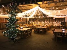 a large room with tables and chairs covered in white fabric, lit by christmas lights