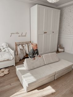 a baby sitting on top of a couch in a room with white walls and wooden floors