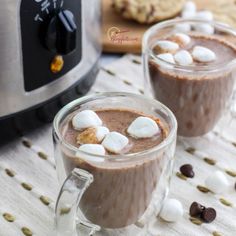 two mugs filled with hot chocolate and marshmallows next to an electric toaster