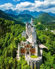 an aerial view of a castle in the middle of trees with mountains in the background