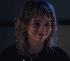 a close up of a person wearing a black shirt and smiling at the camera with long curly hair