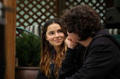 two people sitting next to each other in front of a potted plant