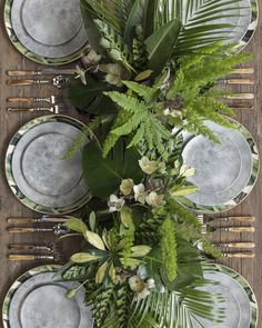 the table is set with silver plates and green plants