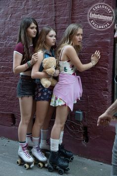 three girls are standing on roller skates and one girl is holding a teddy bear