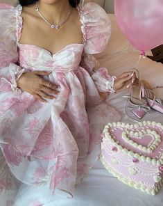 a woman in a pink dress sitting next to a heart shaped cake