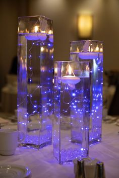 two clear vases filled with lit candles on top of a white tablecloth covered table