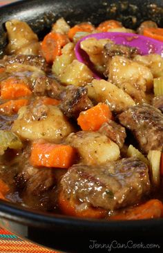 a bowl filled with meat and vegetables on top of a checkered table cloth next to a spoon