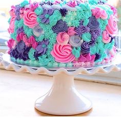 a multicolored cake sitting on top of a white plate next to a window