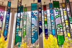 several colorful stained glass pieces hanging from the ceiling in front of a window with trees outside