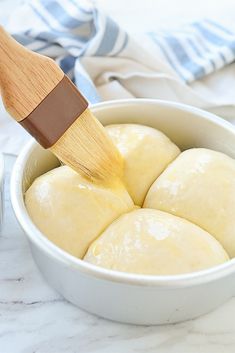 a wooden spatula being used to spread the dough into a white bowl on a marble countertop