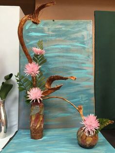 two vases filled with flowers on top of a blue table next to a painting