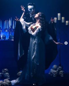 a couple dressed up as dracula and bride kissing in front of skulls on the ground