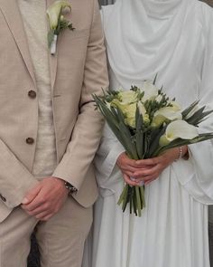 a bride and groom standing next to each other in front of a wall holding flowers