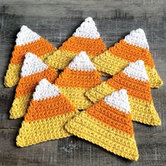 crocheted candy corn cozies are arranged on a wooden surface, ready to be used as decorations