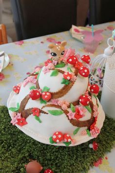 a decorated cake sitting on top of a green tablecloth covered in flowers and mushrooms