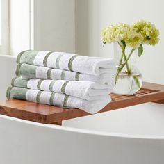 a stack of white towels sitting on top of a wooden shelf next to a vase with flowers