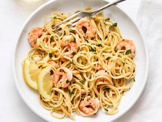 a plate of pasta with shrimp, lemon and parsley on the side next to a fork