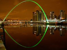 a large green arch is in the middle of a body of water with city lights behind it