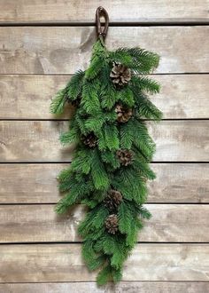 pine cones and evergreen needles hang from a hook on a wood planked wall, decorated with metal hooks