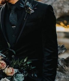 a man in a tuxedo holding a bouquet of flowers and greenery with his face close to the camera