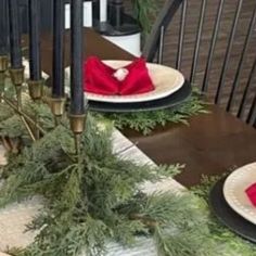 the table is set for christmas dinner with red napkins and evergreen garland on it