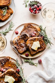 french toast topped with butter and cranberries on a plate next to two glasses of wine