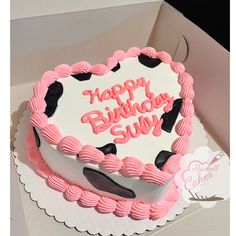 a heart shaped birthday cake with pink frosting and black dots on the top, sitting in a box